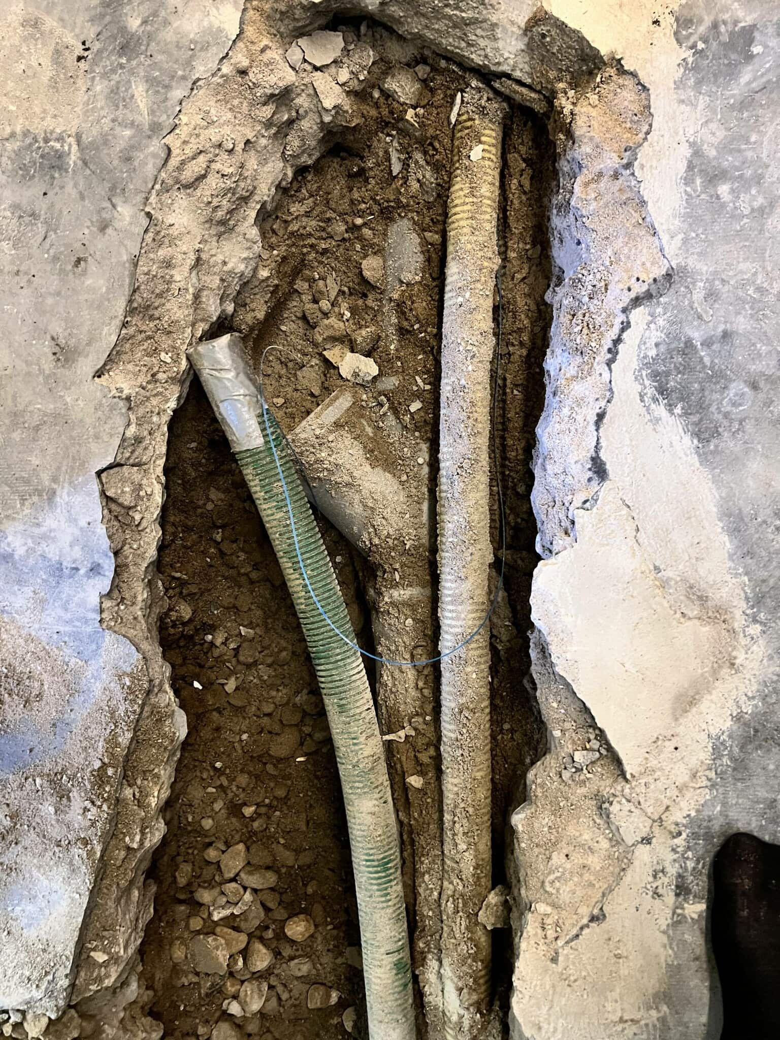 Ett öppet hål i golvet avslöjar rör och grus, vilket indikerar pågående renovering eller reparation av underliggande installationer.