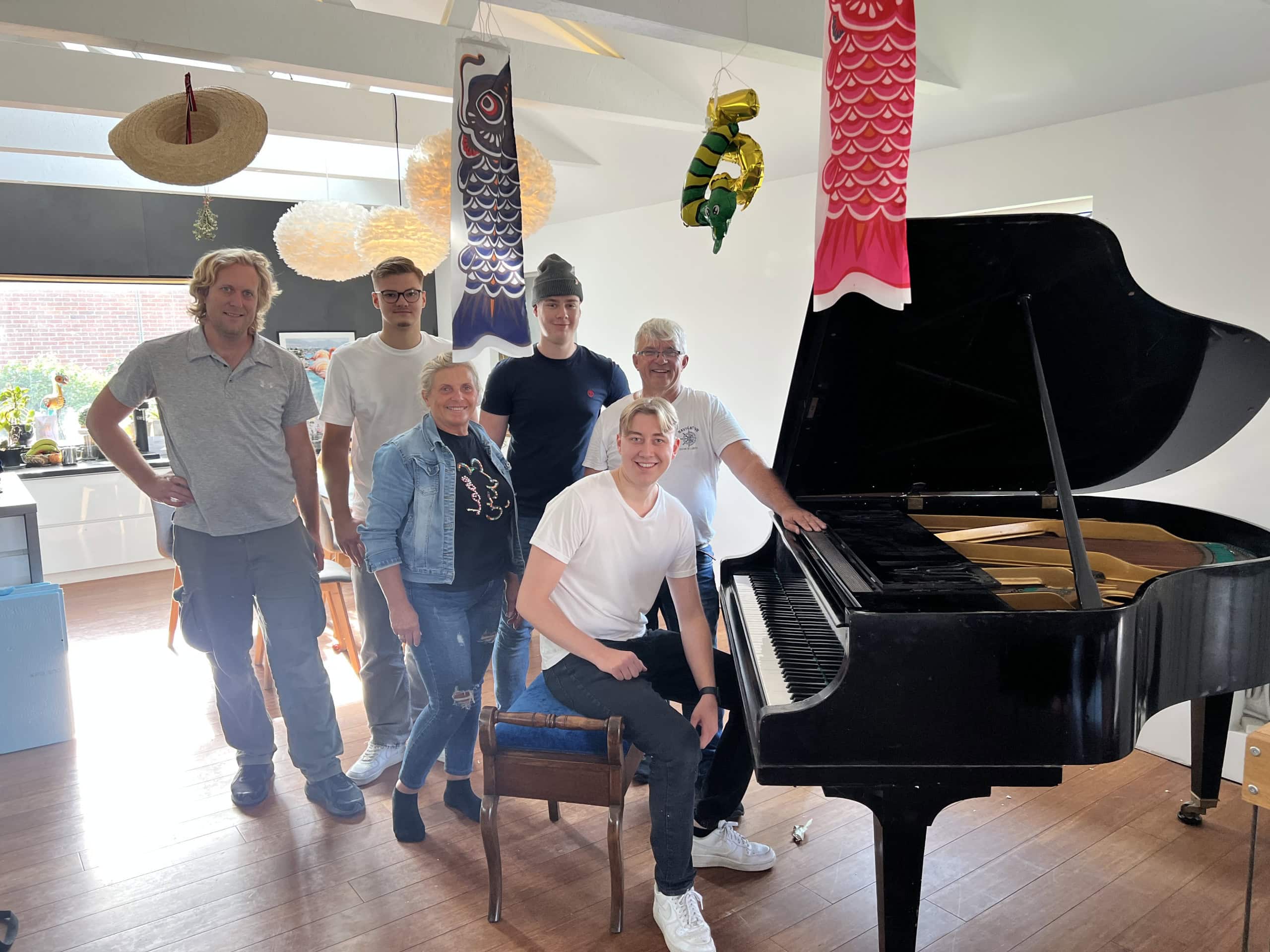 En grupp människor poserar i ett stilrent, ljust rum med en flygel och dekorativa fiskar hängande från taket.